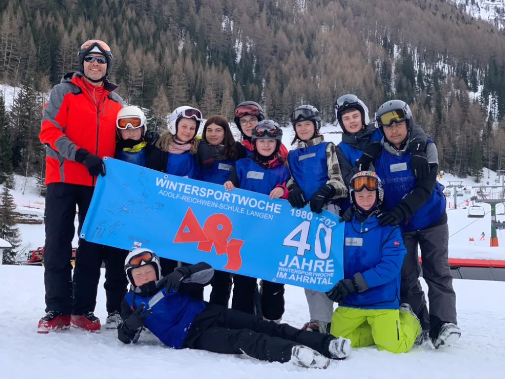 Eine Gruppe posiert mit dem Banner, einige liegen im Schnee davor.